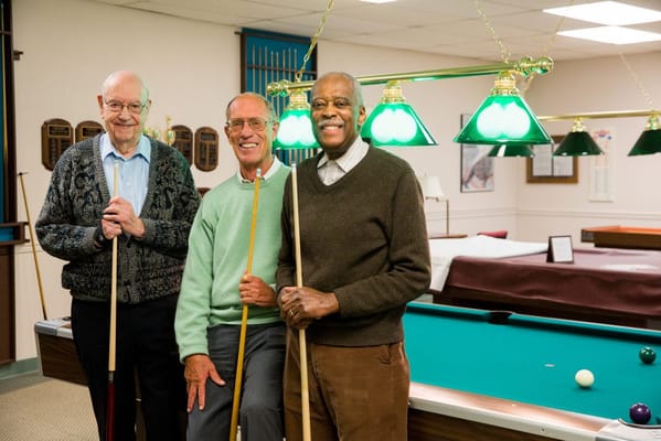 Three residents posing with pool cues in an activity room