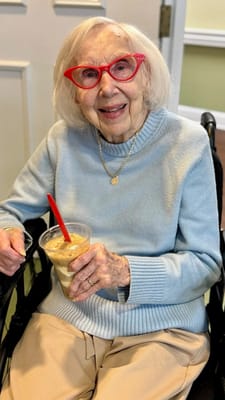 A smiling resident enjoying a drink in a wheelchair