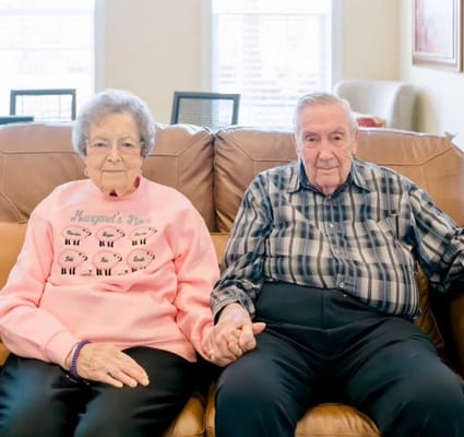 Two residents sitting together on a couch, holding hands