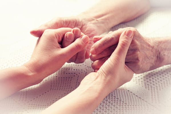 Hands of a caregiver and a resident holding each other
