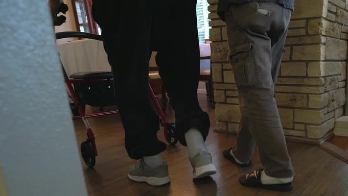 Two residents walking with assistance in a facility interior
