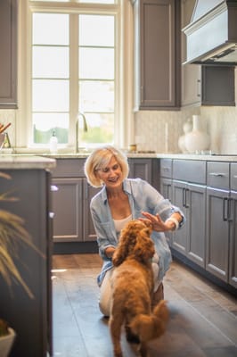 A senior woman playing with a dog in a kitchen