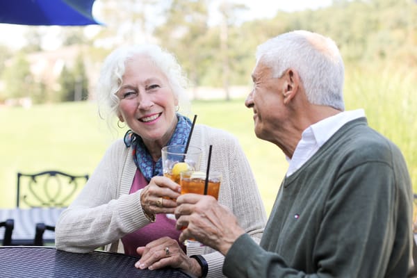 Two seniors enjoying drinks outdoors in a garden setting