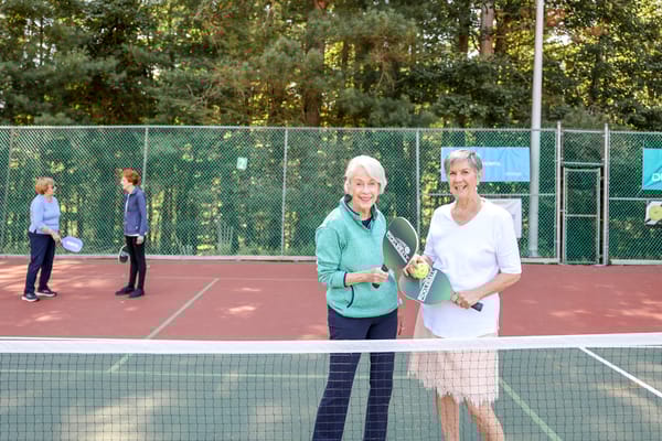 Two women holding paddles on a tennis court with other players behind
