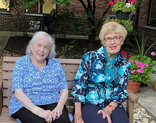 Two women sitting on a bench in a garden