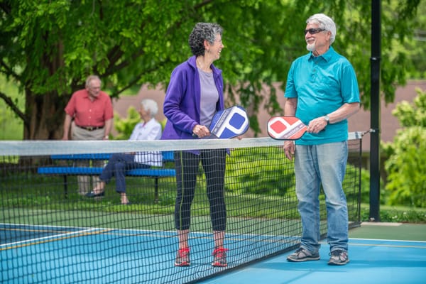Two residents smiling and holding pickleball paddles