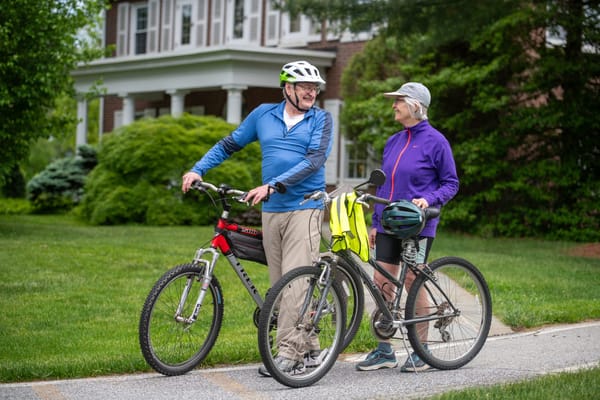 Two seniors biking outside a facility on a sunny day