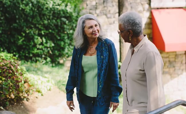Two women walking and chatting in a garden area