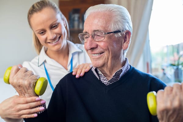 A caregiver assisting an elderly man with weights