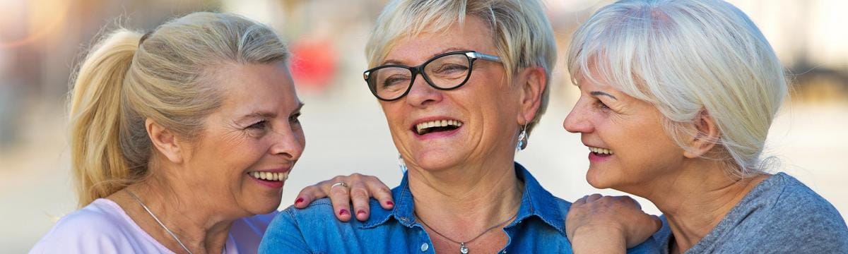 Three senior women laughing together outdoors