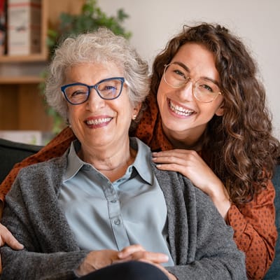 A smiling woman embraces a senior resident in a cozy setting