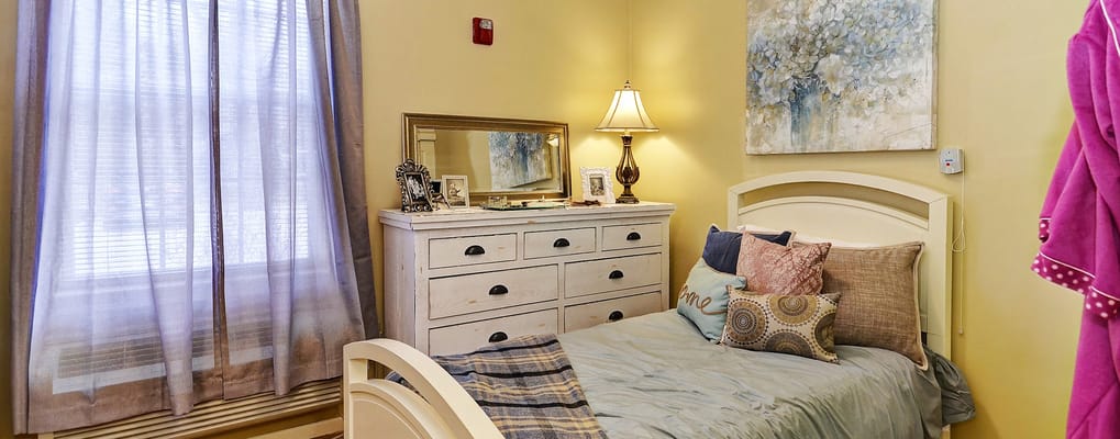 Cozy bedroom with a bed and dresser in a senior living facility.