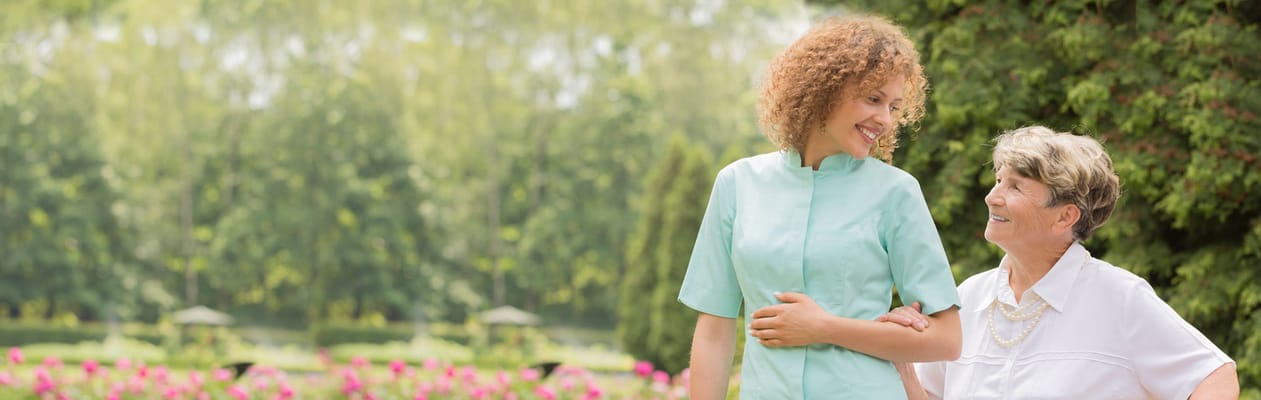 A caregiver assisting a senior woman in a garden