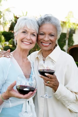 Two smiling women holding glasses of wine outdoors