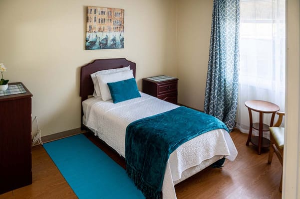 Well-decorated private resident room with bed and chair