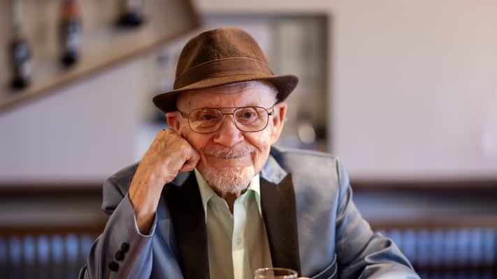 A smiling elderly man in a stylish outfit at a table