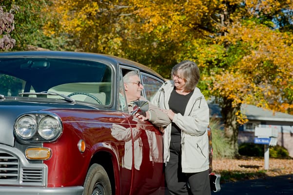 A senior man and woman interacting by a classic car