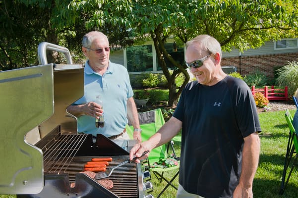 Two men grilling outdoors in a garden setting