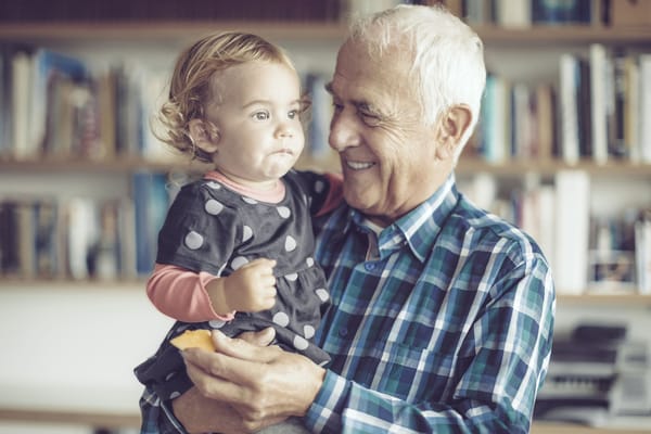 An elderly man happily holding a young girl.