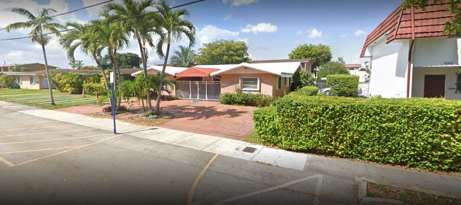 Front entrance of Angeles ALF Inc. with landscaping and palm trees.