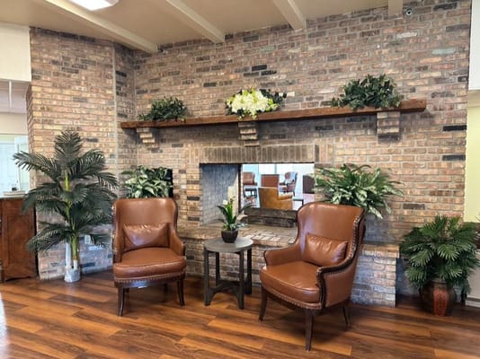 Two brown leather chairs in a lounge area with a stone fireplace and plants.
