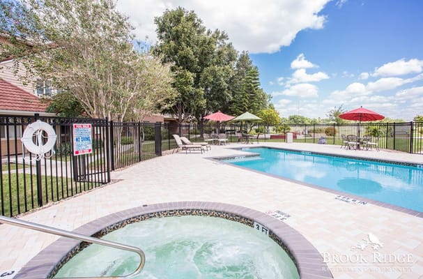 Outdoor pool and hot tub area with lounge chairs and umbrellas