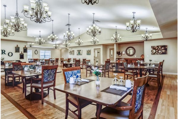 Brightly lit dining room with wooden tables and chandelier, floral centerpieces