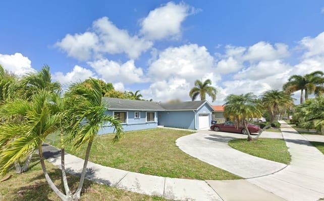 Exterior view of Chanel Nursing Care ALF with palm trees and driveway.