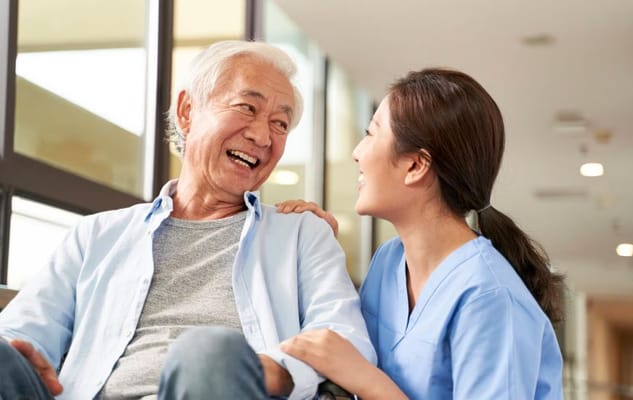 Senior man laughing with a caregiver in a hallway.