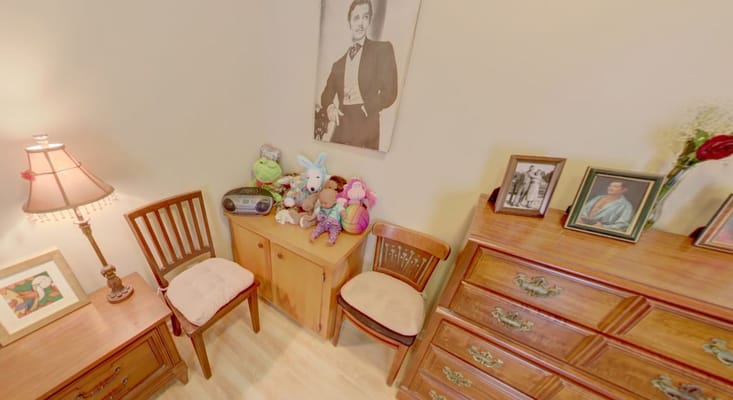 A corner of a room with wooden furniture, a lamp, stuffed toys, and framed photos
