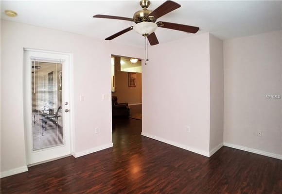 A spacious living room with a ceiling fan and an entry door.