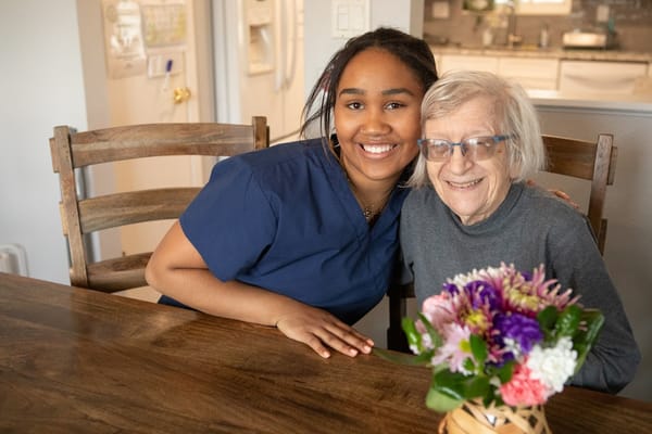 A caregiver sitting with an elderly resident at a dining table