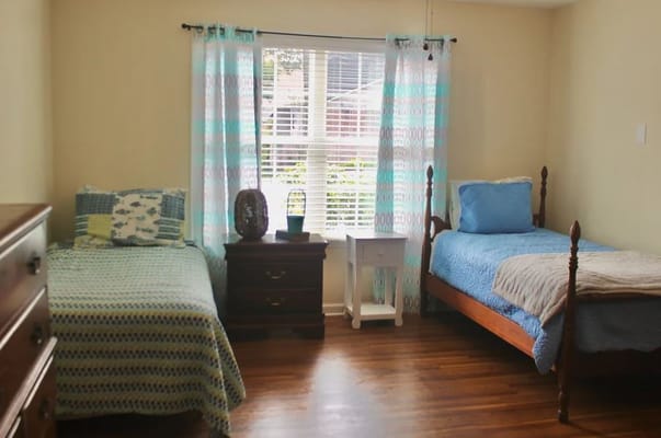Two twin beds in a well-lit bedroom with colorful curtains.