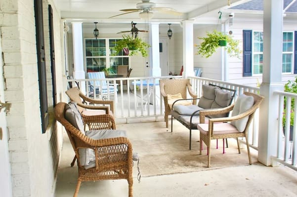 Seating area on the porch with wicker chairs and hanging plants.