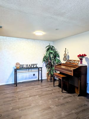 A common area featuring a piano, decorative plants, and a motivational sign.