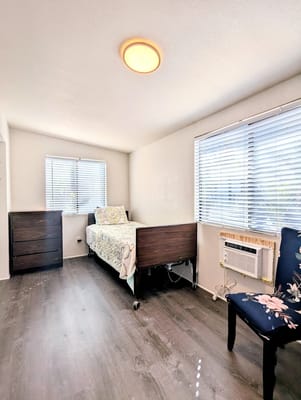 Bright bedroom with a bed, dresser, and patterned chair.