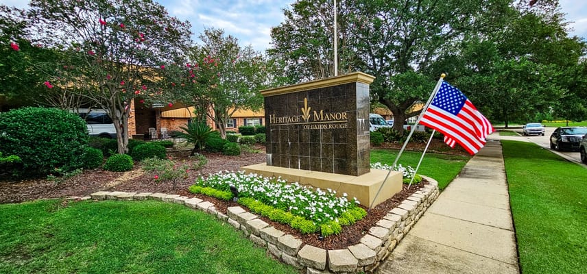 Signage of Heritage Manor of Baton Rouge with American flag and landscaping