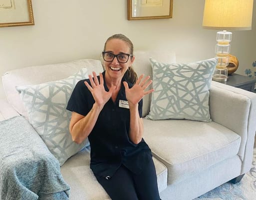 Staff member smiling and waving from a sofa in a cozy living room