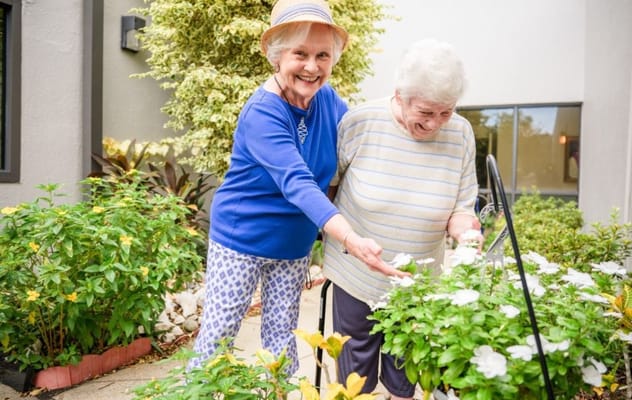 Two elderly women tending to flowers in a garden