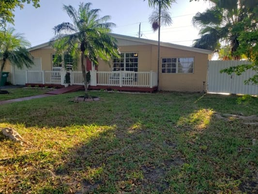 Sunlit front yard with palm trees and white railing at Jolly Home Inc.