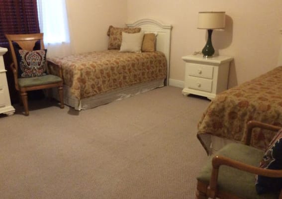 A cozy shared room with two beds, a lamp, and a chair.