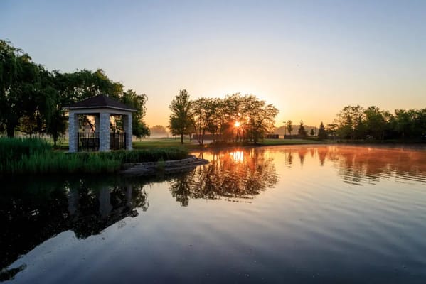 A gazebo beside a calm lake reflecting the morning sun.