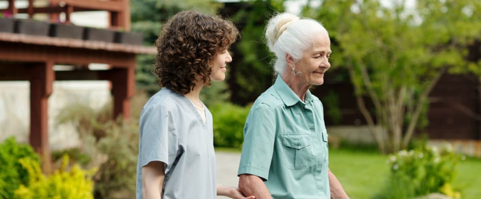 A caregiver walking alongside a senior resident in a garden.