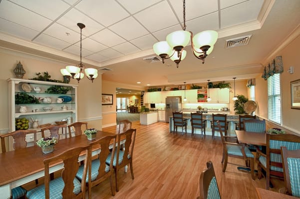 Bright dining area with wooden tables and chairs, featuring a kitchenette.