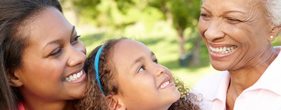 A senior woman smiles joyfully with her daughter and granddaughter outdoors.