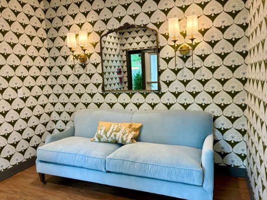 A blue couch against a patterned wall with a mirror and sconces