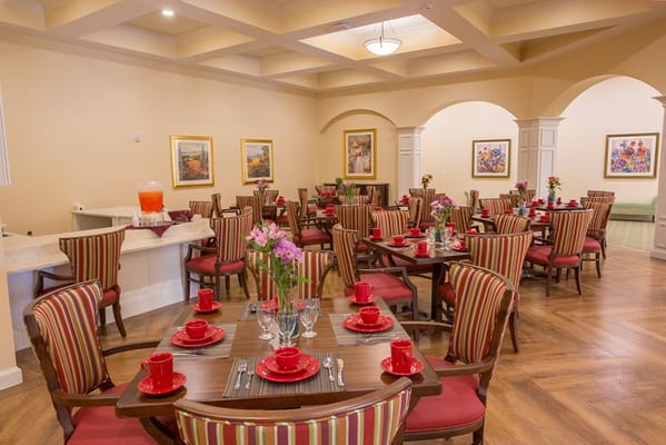 Cozy dining room setup with red and striped chairs and tables adorned with plates and flowers.