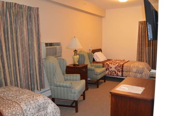 Interior of a cozy room with two armchairs, a bed, and a dresser.