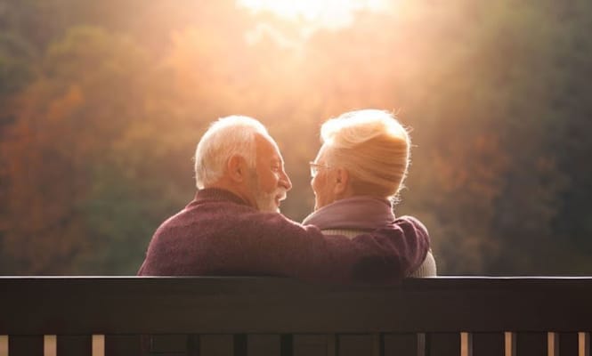 Elderly couple embracing on a bench during sunset