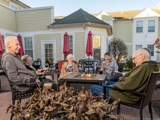 Group of seniors sitting around a fire pit, laughing and enjoying drinks.